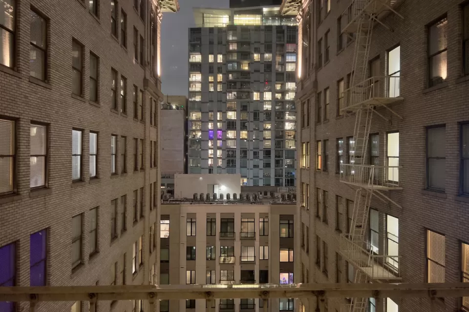 View from between tall white brick buildings in evening in downtown Los Angeles with modern office building across street.